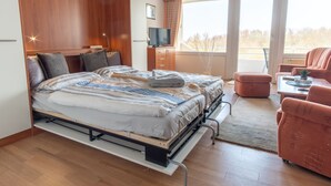 Ein modernes Schlafzimmer mit Bett, Fernseher, einer Couch und einem Balkon.