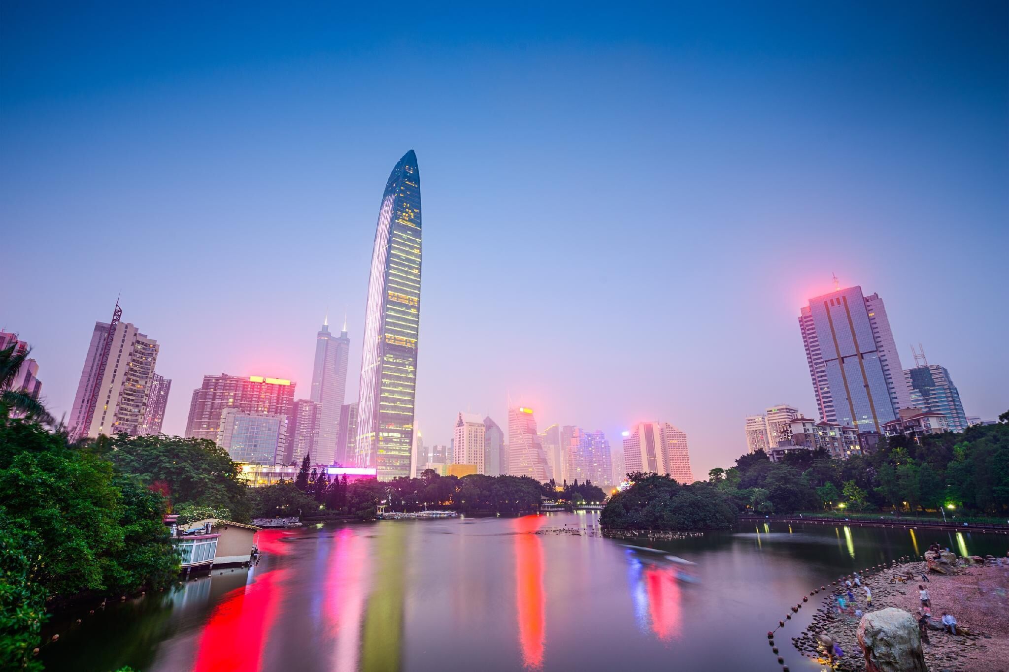 A cityscape with a prominent skyscraper, a calm river, and surrounding greenery.