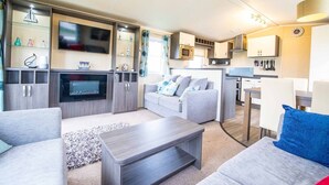 Ein modernes Wohnzimmer mit Flachbildfernseher, grauen Sofas, einem Couchtisch und einer Küchenzeile mit Mikrowelle und Schränken.