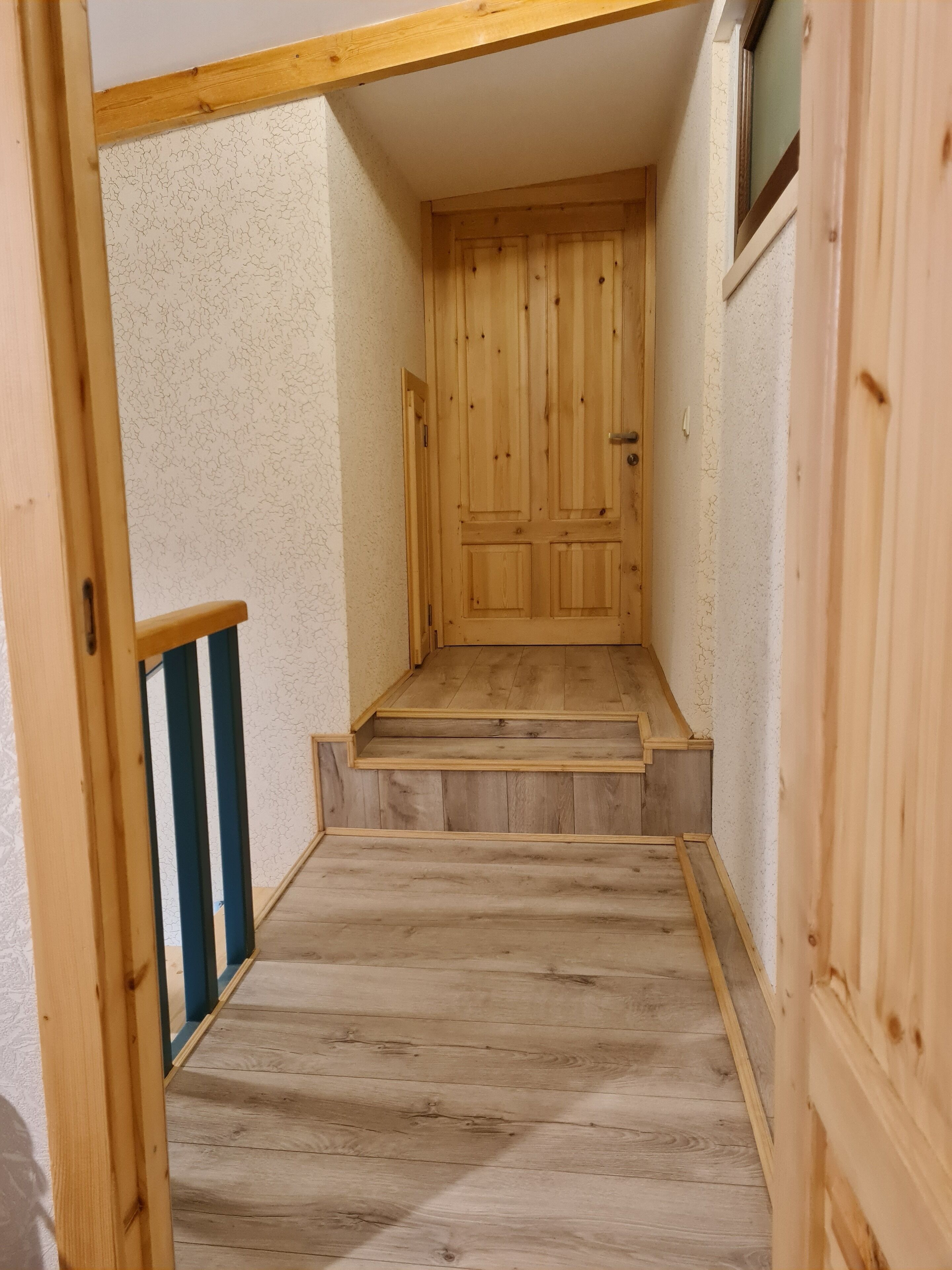 A wooden staircase leading to a door in a hallway with textured walls.