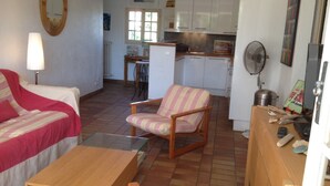 A compact living space with a bed, a striped armchair, a wooden table, and a kitchenette in the background. - Le Tassergal : Port Gimaud / St Tropez, 2 Chambres vue sur L'eau (Grimaud)