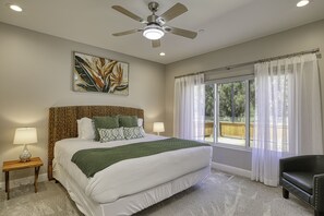 Une chambre avec un grand lit, un ventilateur de plafond, une fenêtre avec des rideaux et une vue sur l’extérieur.