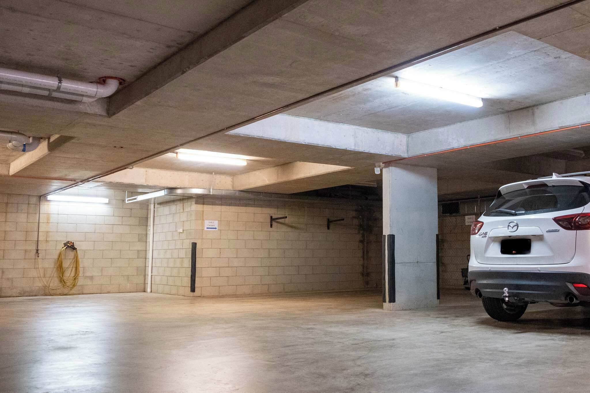 A parking garage with concrete walls and a white car parked in the foreground.