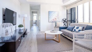 A modern living room with a sofa, coffee table, and TV. There is a hallway leading to another room. - Live like a local In the heart of Moffat Beach (Moffat Beach)