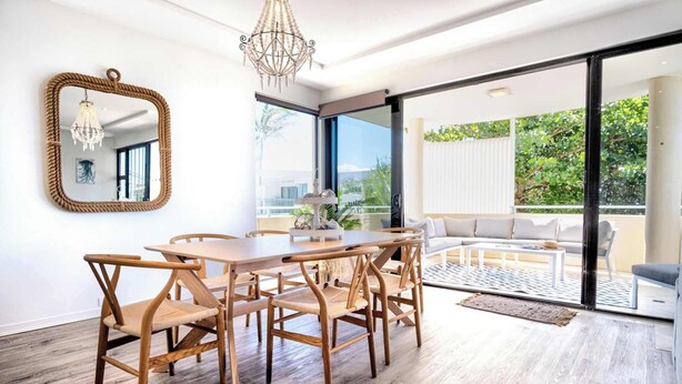A modern dining area with a wooden table and chairs, a chandelier, and a large mirror on the wall. - Live like a local In the heart of Moffat Beach (Moffat Beach)