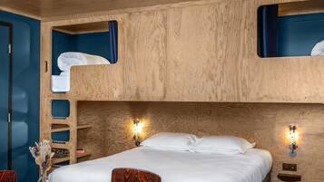 Een slaapkamer met een stapelbed, een houten hoofdbord, een nachtkastje met een tijdschrift en een vaas met gedroogde bloemen.