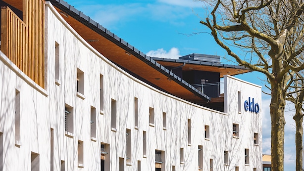 Un edificio moderno con fachada blanca y detalles de madera, con varias ventanas y el letrero 'ekdo' a la vista.
