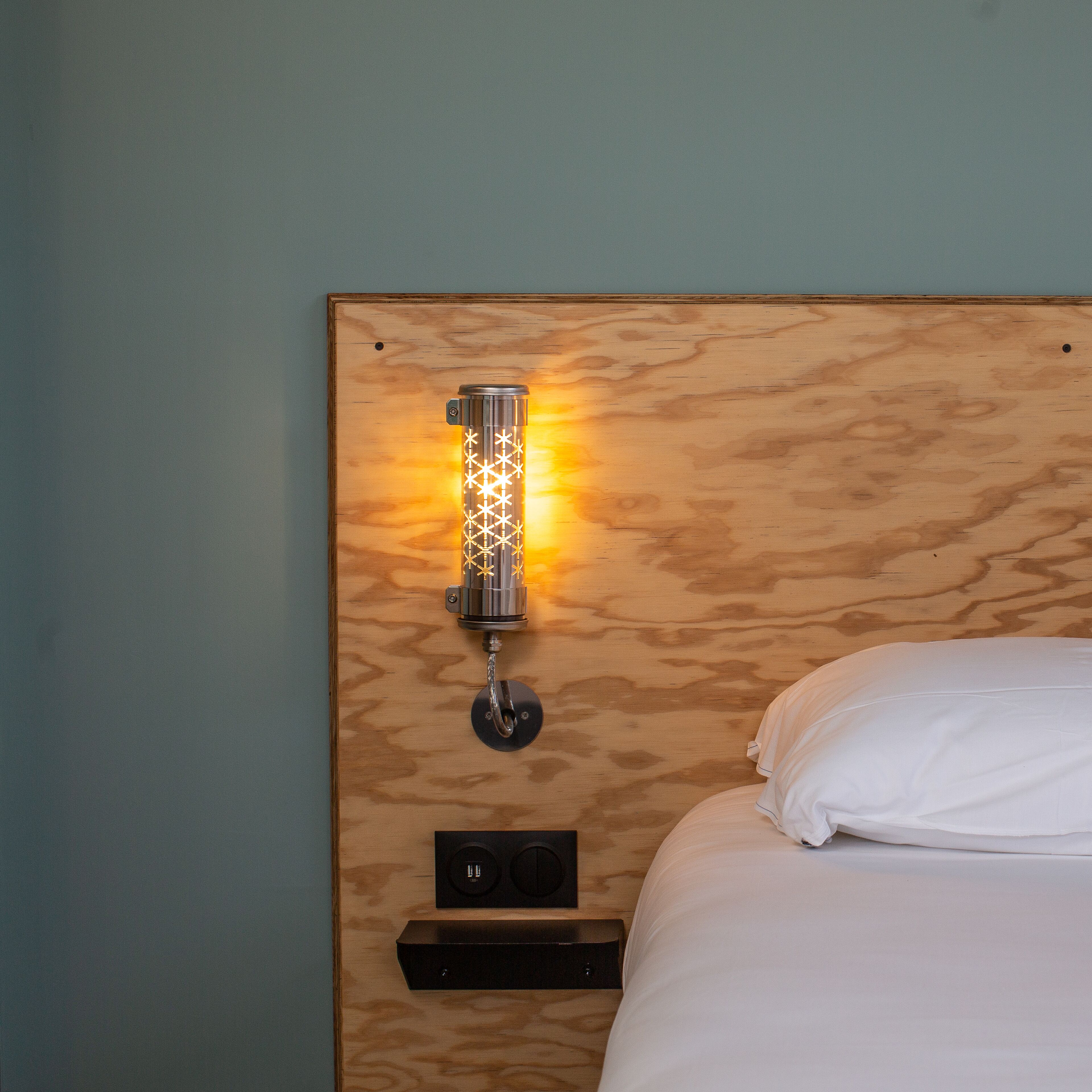 A wooden headboard with a wall-mounted light fixture and a power outlet below it.