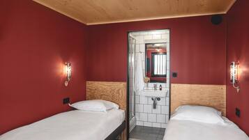 Una camera d'albergo con due letti singoli, soffitto in legno, pareti rosse e bagno con specchio e lavandino.