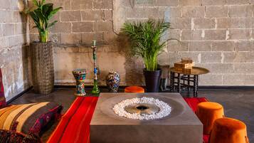 Un área de estar moderna con una mesa de centro de hormigón, plantas en macetas, un narguile decorativo y una pequeña mesa de madera con cajas apiladas.