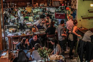 Una cocina de restaurante concurrida, con chefs preparando comida y comensales sentados en mesas.