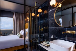 Una habitación de hotel moderna con una cama grande, un baño independiente con bañera y un espejo amplio.
