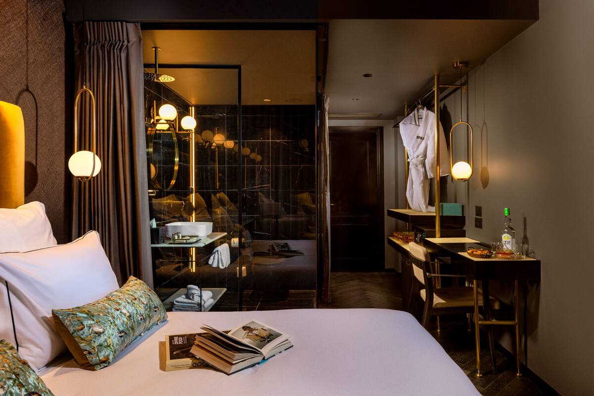Ein Hotelzimmer mit Bett, Schreibtisch, Spiegel und einem durch eine Glaswand abgetrennten Badezimmer.