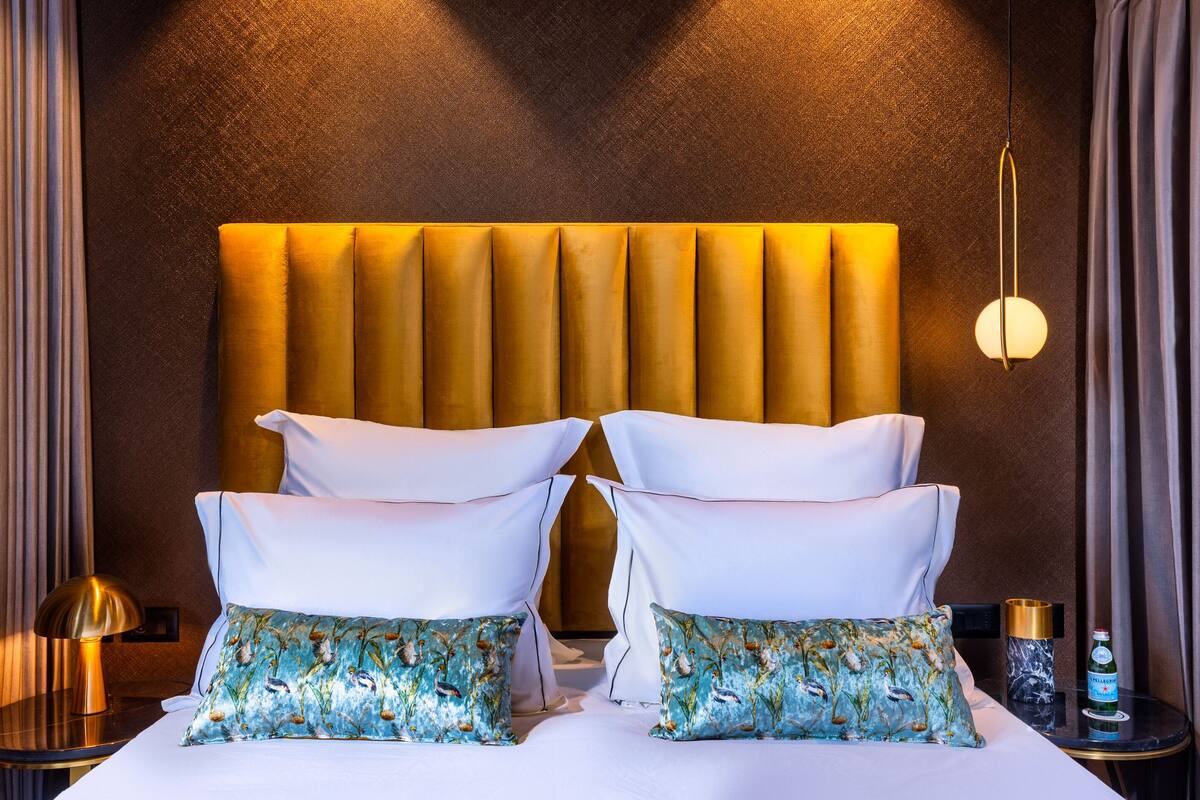 Ein Hotelzimmer mit einem großen Bett, einem Kopfteil, einem Nachttisch mit Lampe und einem Beistelltisch mit einer Flasche.
