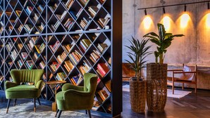 A cozy reading area with a bookshelf, two green armchairs, and two large potted plants. - Brown Machne Yehuda (Jerusalem)