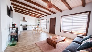 Ein modernes Wohnzimmer mit Holzboden, einer Couch, einem Couchtisch und einer Küche im Hintergrund.