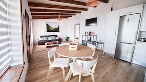 Eine moderne Küche mit einem Edelstahl-Kühlschrank, einem Holzespeisetisch mit weißen Stühlen und einer Holzzahlendecke mit sichtbaren Balken.