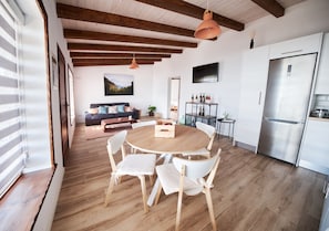 A modern kitchen with a stainless steel refrigerator, wooden dining table with white chairs, and a wooden ceiling with exposed beams.