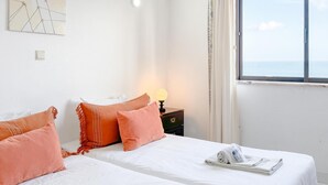 A hotel room with a bed, pillows, a nightstand, a lamp, a window with a view, and a wall art piece. - Tranquility and Sea View at Meia Praia (Lagos)