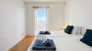 A hotel room with two beds, a window with curtains, a bedside lamp, and a view of the cityscape. - Bright apartment next to main avenue and marina (Lagos)