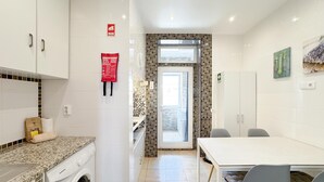 Eine moderne Küche mit integriertem Waschmaschinenanschluss, ein Essbereich mit Tisch und Stühlen und ein Blick durch eine Glastür auf einen Balkon.