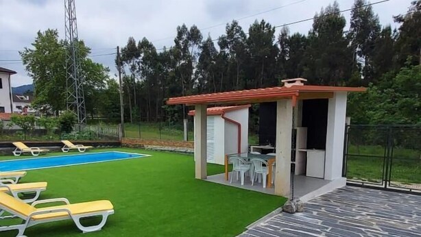 A pool area with artificial grass, lounge chairs, and a small pavilion with a table and chairs.