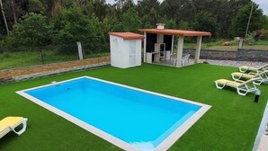 A rectangular pool with a surrounding green artificial grass area, a small covered seating area, and several yellow lounge chairs.