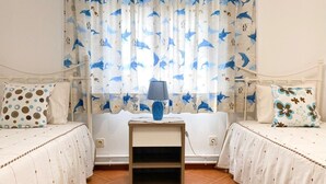 A bedroom with two beds, a nightstand, a lamp, and a window with curtains.