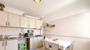 A kitchen with white cabinets, a gas stove, a microwave, and a sink. There is a green basket and a white table with chairs.