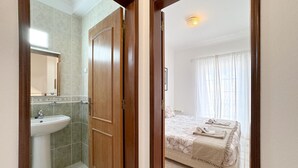 A hotel room with a bathroom, a bed with a floral bedspread, and a window with curtains.