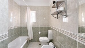 A bathroom with a bathtub, toilet, sink, and shower area.