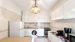 Une cuisine de taille réduite avec des meubles blancs, un lave-linge, une cuisinière et un four à micro-ondes.