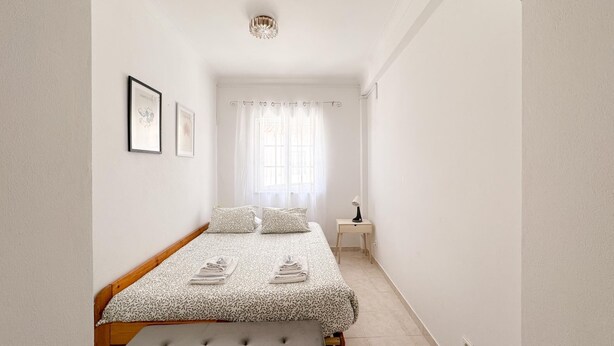 Une chambre à coucher avec un lit, une table de chevet, une lampe et une fenêtre avec des rideaux.