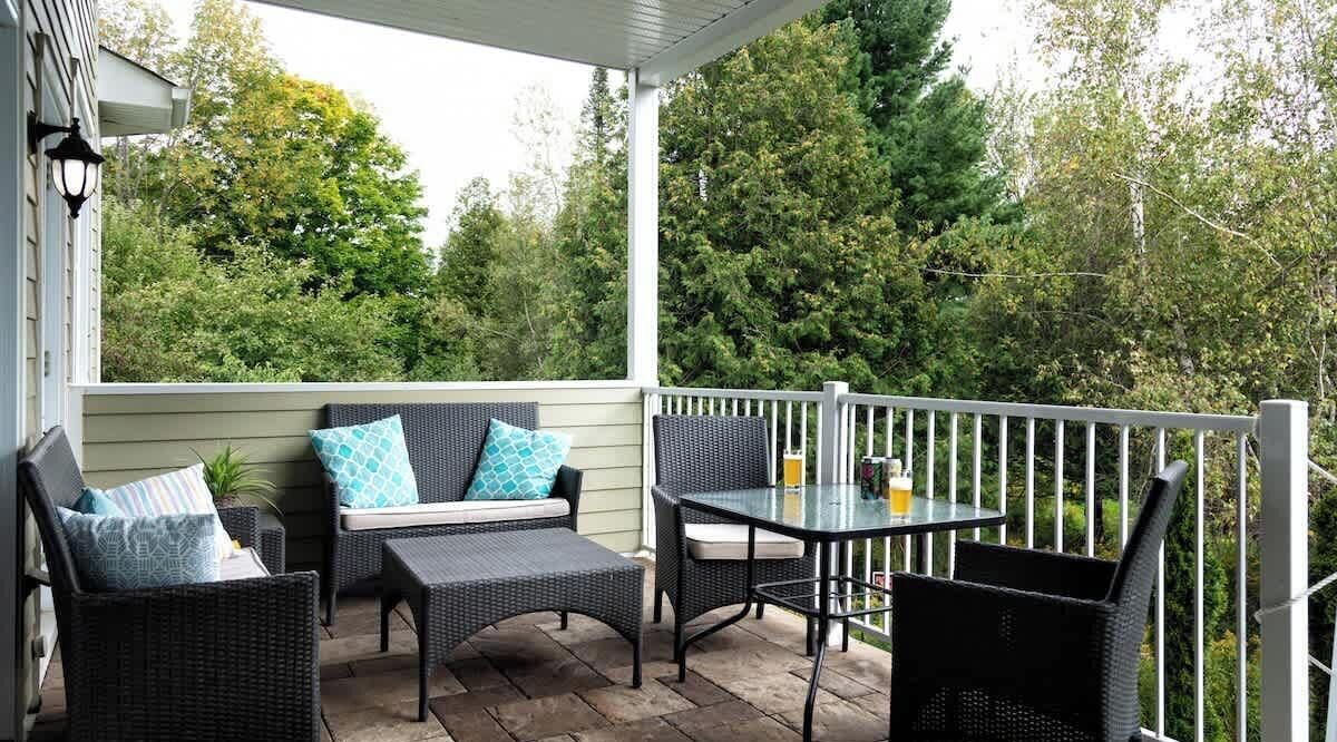 A covered patio with wicker furniture, a table with drinks, and a view of trees.