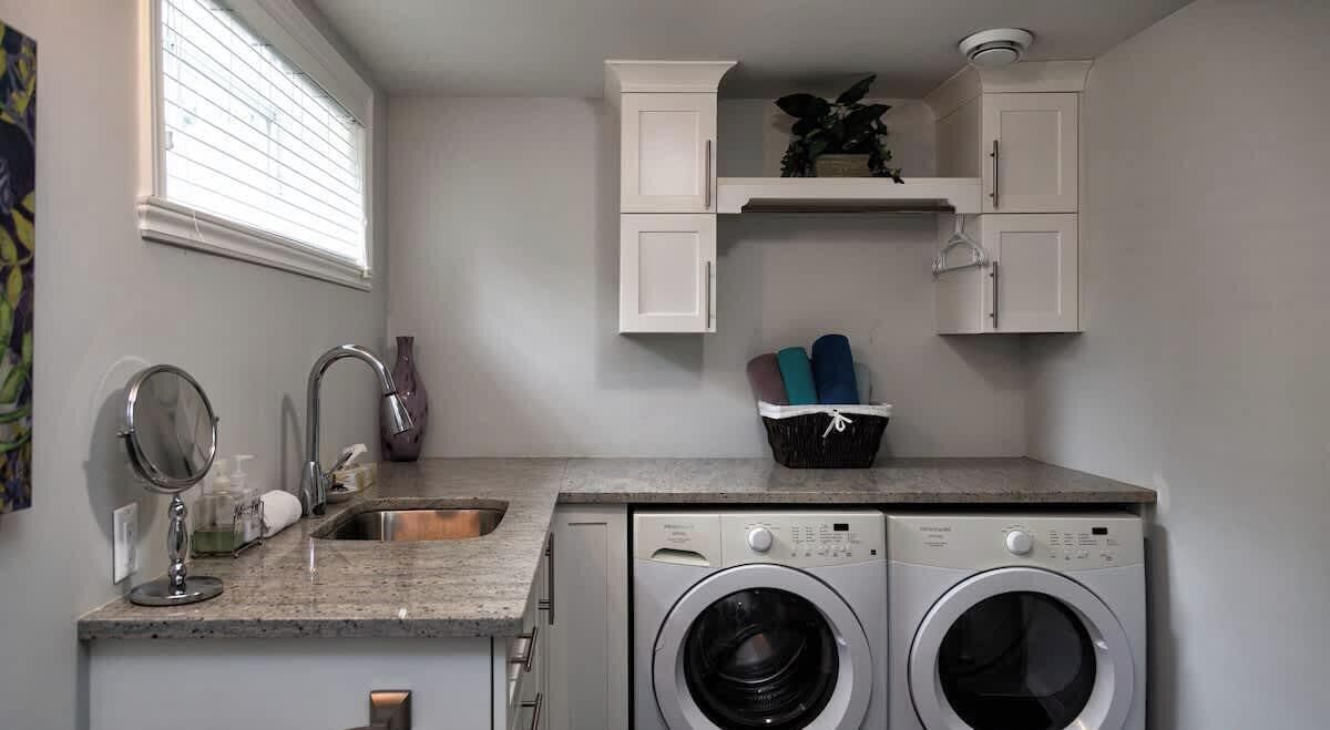 A compact laundry area with a sink, two washing machines, and a small shelf with folded towels.