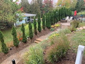Un jardin avec un chemin dallé, des haies bien taillées et un petit abri de jardin.