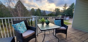 Une terrasse extérieure avec des chaises en osier et une table en verre, entourée d’une rambarde en métal.