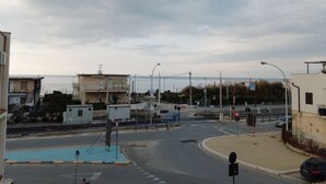 A coastal road with a railway crossing, buildings, and a clear view of the sea. - SEASIDE APARTMENT (Alcamo Marina)
