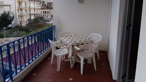 A balcony with a table and chairs, a blue railing, and a view of buildings in the background. - SEASIDE APARTMENT (Alcamo Marina)