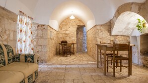 Une pièce aux murs de pierre, aménagée avec un canapé, une table et des chaises, et dotée d’une porte en arc de cercle et d’un luminaire suspendu.