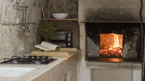 Une cuisine avec un mur en pierre, un poêle à bois, un four grille-pain et un feu qui crépite dans la cheminée.