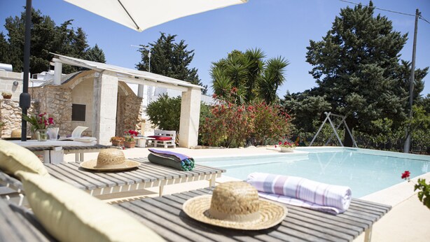 Un espace aménagé au bord de la piscine, avec des chaises longues, un bâtiment en pierre et une vue sur la piscine.