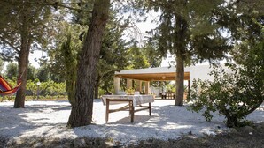 Un espace extérieur abrité, avec une table et des bancs, entouré d’arbres et agrémenté d’un hamac.