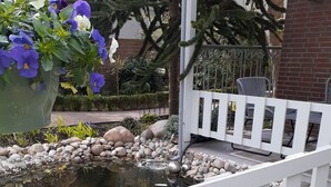 A garden with a pond, white railing, and potted flowers. - Blaue Welle - Gemütlichkeit mit Stil (Varel)