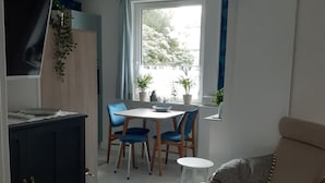 A room with a dining table and chairs, a sofa, a TV, and a window with plants. - Blaue Welle - Gemütlichkeit mit Stil (Varel)