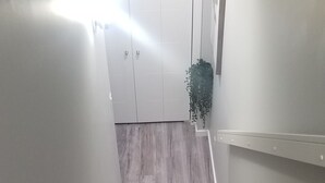 Una escalera alfombrada con piso de madera en la parte superior, paredes blancas y una planta colgante.