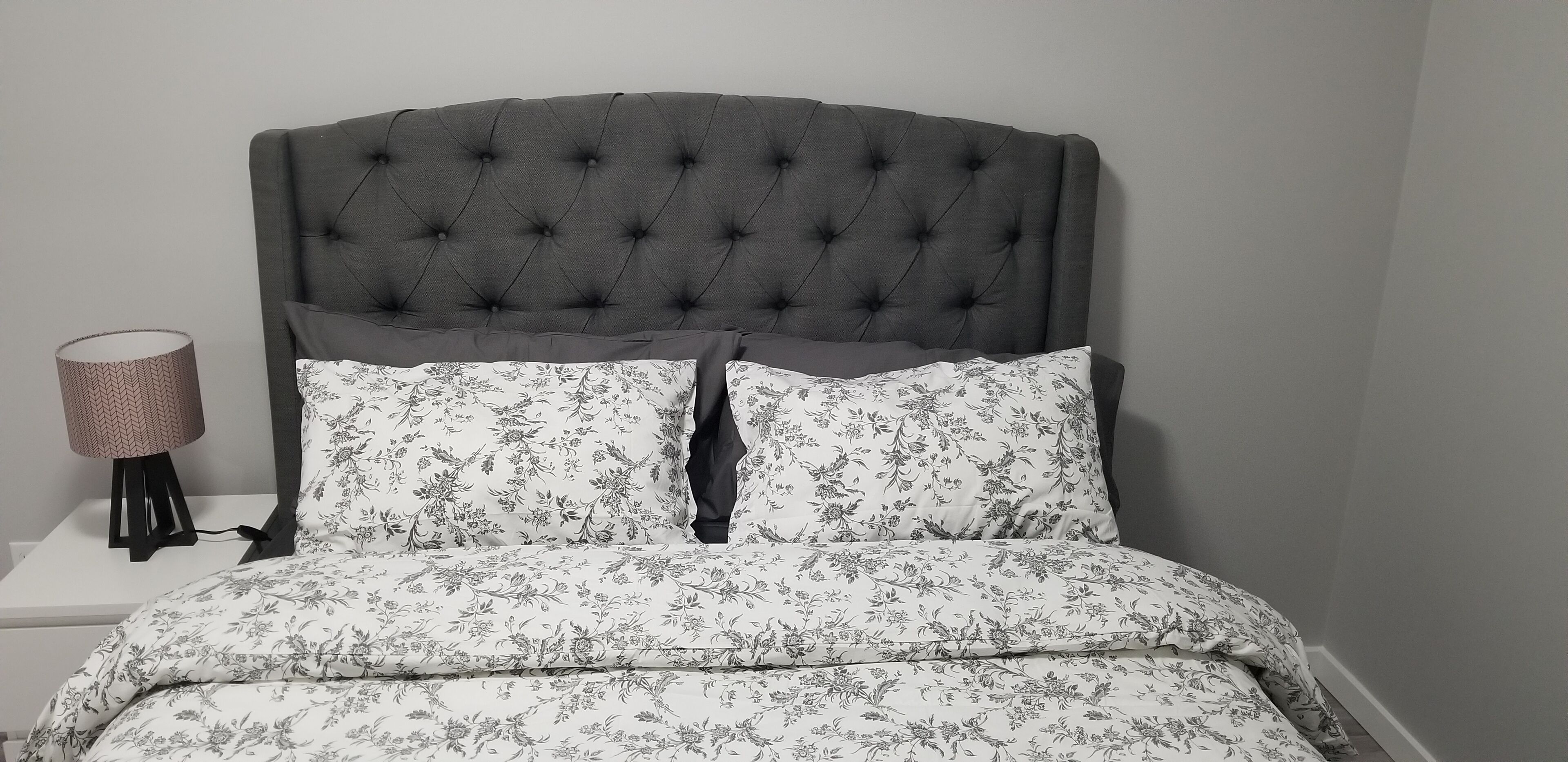 Una cama con cabecera capitonada, ropa de cama floral y una lámpara de noche.
