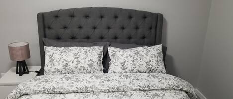 Una cama con cabecera capitonada, ropa de cama floral y una lámpara de noche.
