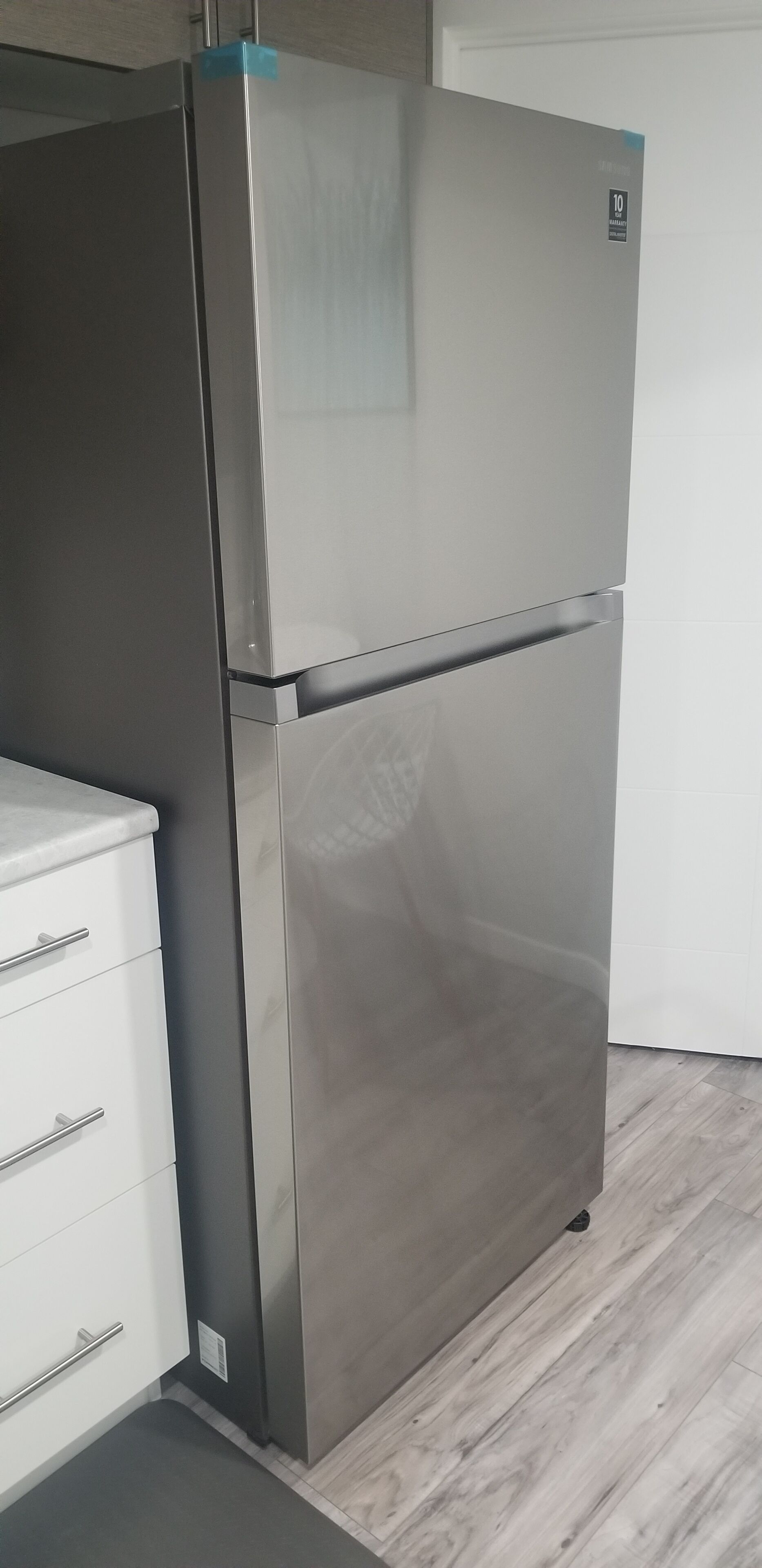 Un refrigerador de acero inoxidable en una cocina con armarios blancos y piso de madera.