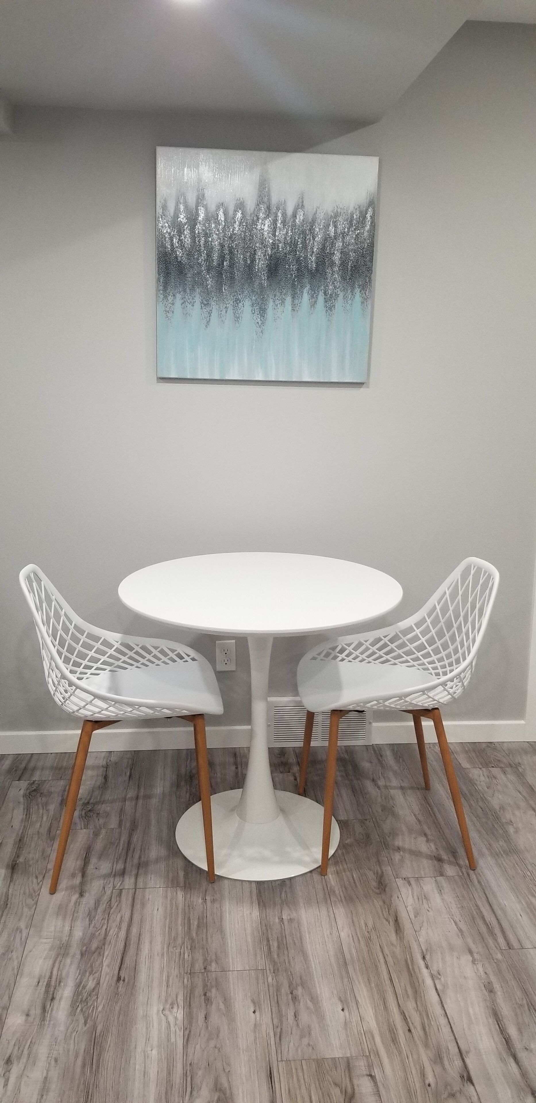Un coin repas avec une table ronde blanche, deux chaises blanches aux pieds en bois et un sol gris.
